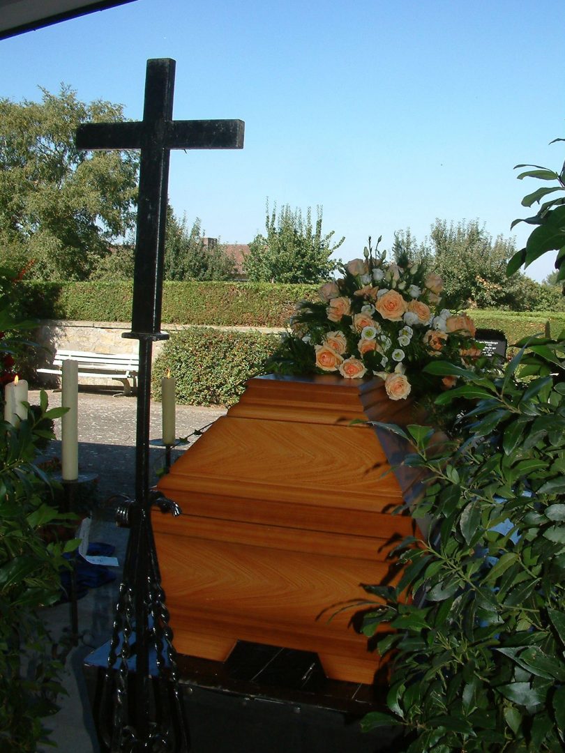 Ein aufgebahrter Sarg mit Blumenschmuck und weissen Kerzen und einem Vortragekreuz