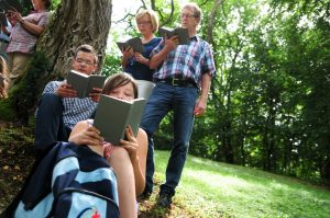 Eine Familie sitzt unter einem Baum und betet aus dem Gotteslob