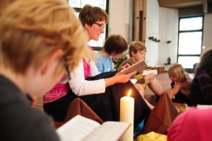 Eine Kindergottesdienstleiterin betet aus dem Gotteslob mit Kindern um eine brennende Kerze