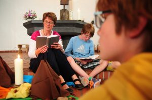 Eine Kindergottesdienstleiterin betet aus dem Gotteslob mit Kindern um eine gestaltete Mitte