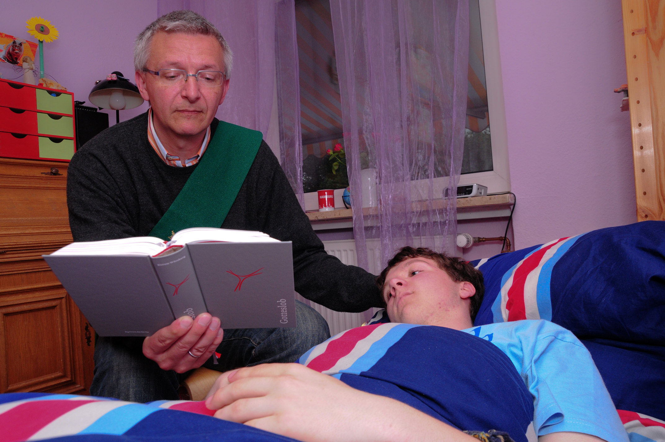 Ein Diakon sitzt am Bett eines kranken Jungen und betet mit ihm vor dem Empfang der Krankenkommunion
