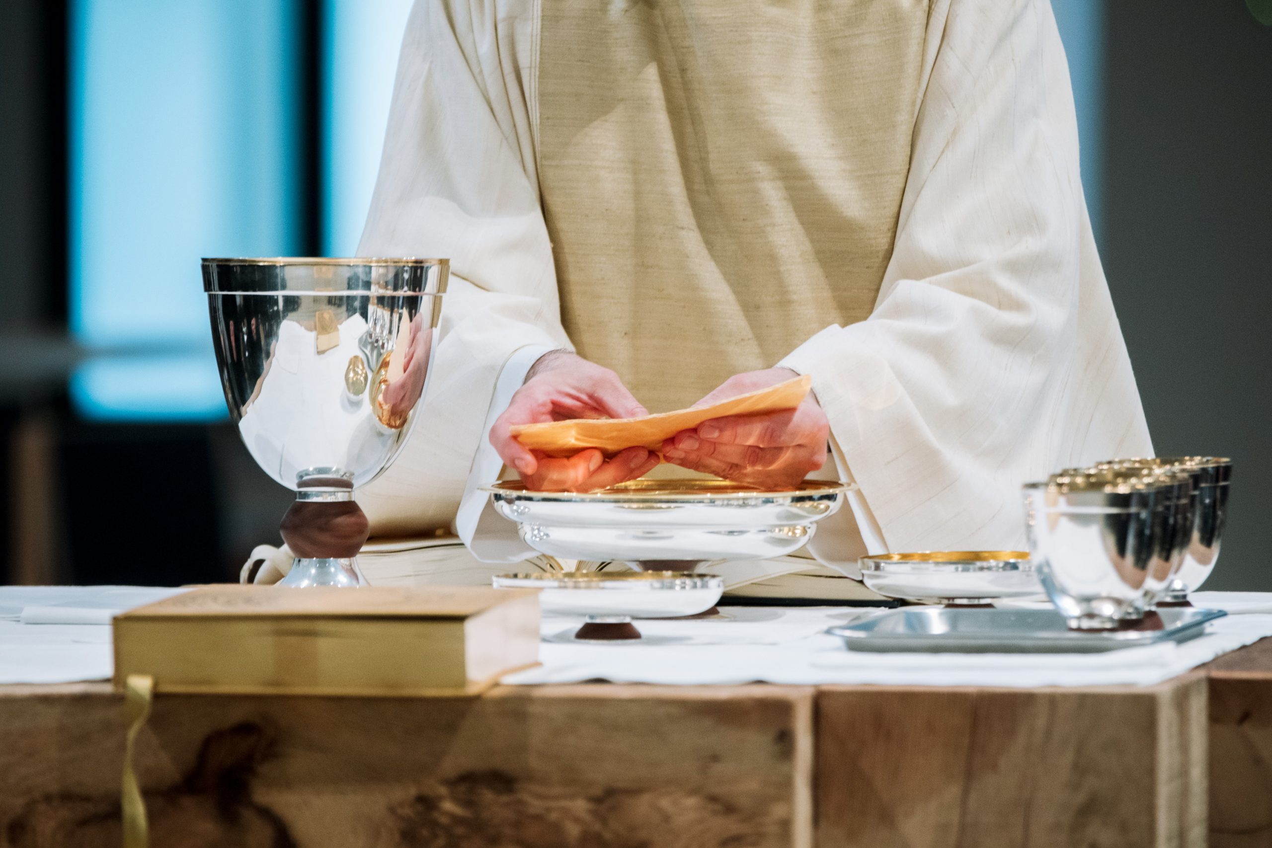 Der Priester bricht das Brot, auf dem Altar weitere Schalen und Kelche