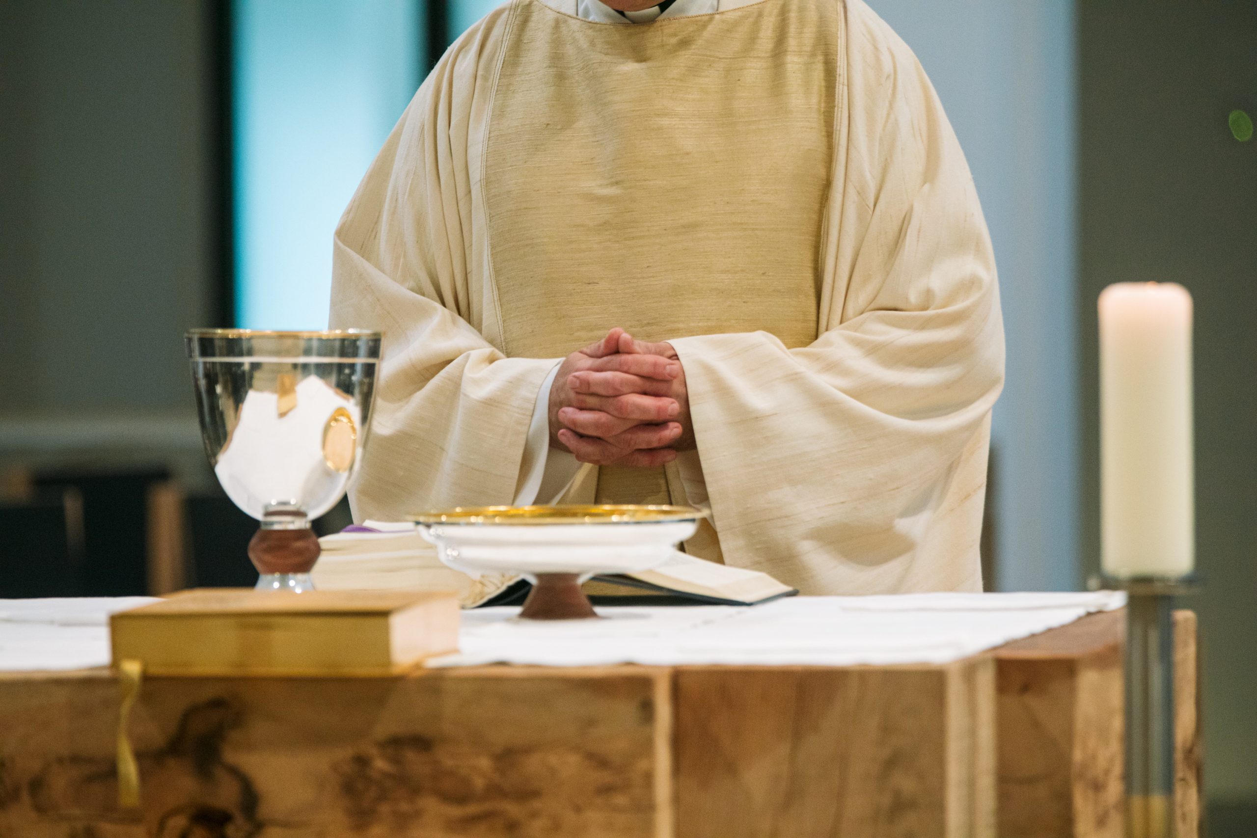 Der Priester steht am Altar, auf dem Kelch und Schale stehen, Messbuch und Evangeliar liegen