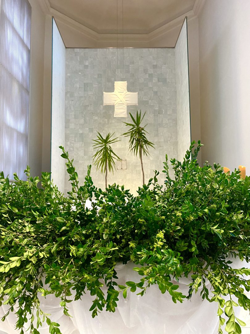 Palmzweige und Palmen unter einem weiss verhuellten Kreuz