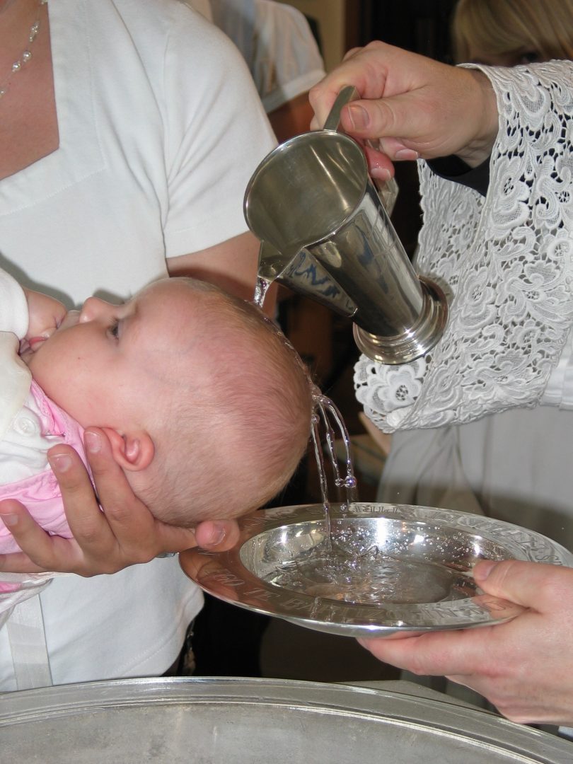 Ein Kleinkind wird mit Kaennchen und Schale mit Wasser uebergossen und getauft