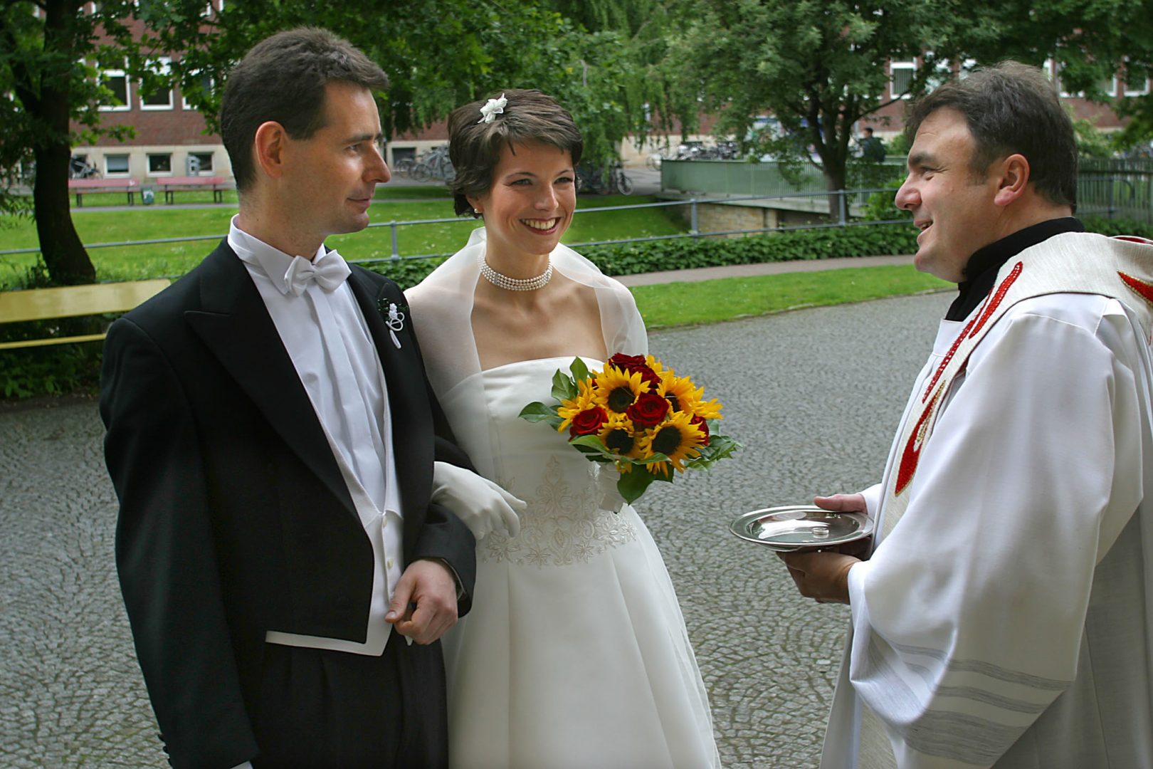 Ein Brautpaar steht mit einem Priester vor der Kirche bevor die Trauung beginnt