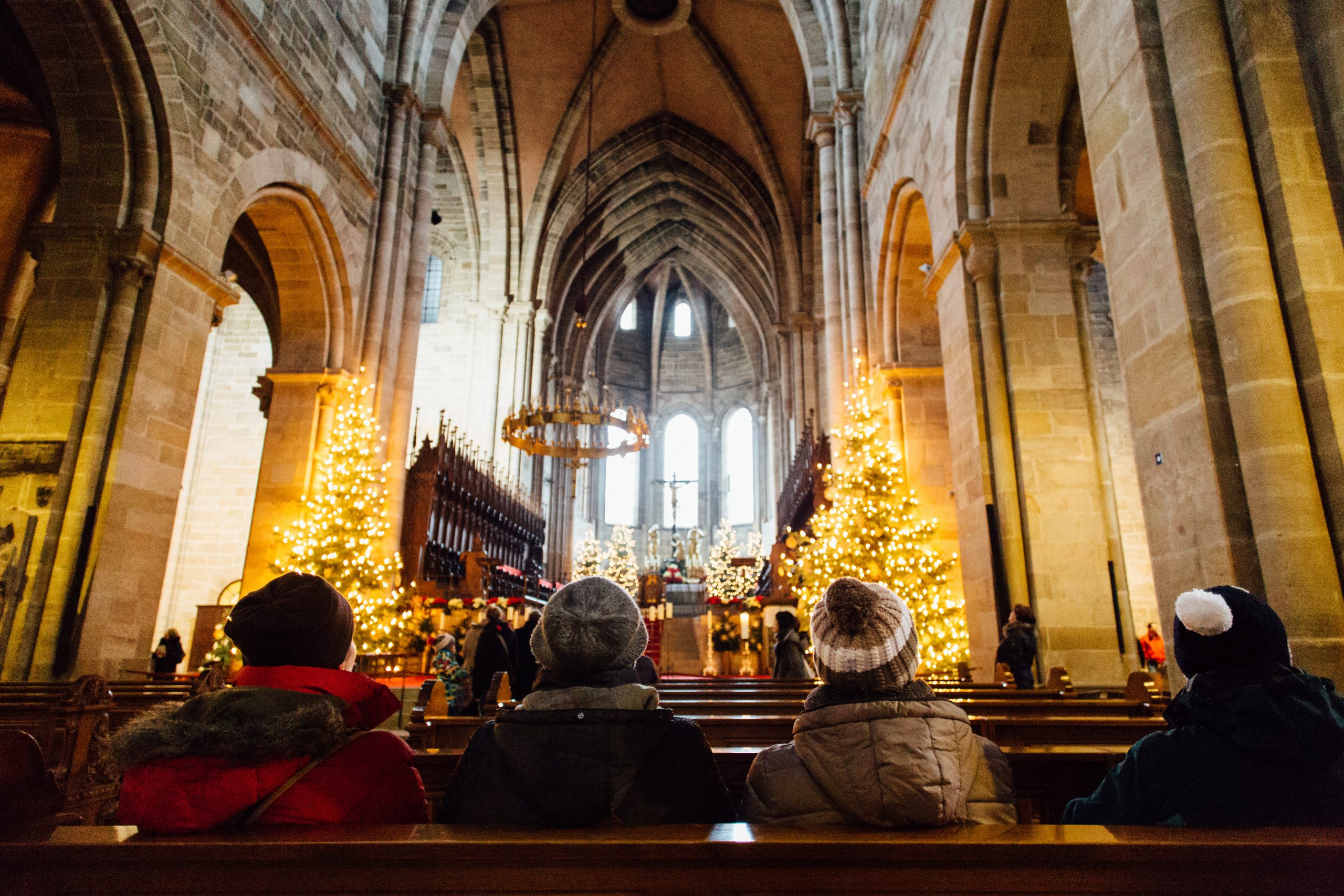 Glaeubige sitzen in einer Kirchenbank vor dem weihnachtlich geschmueckten Altarraum