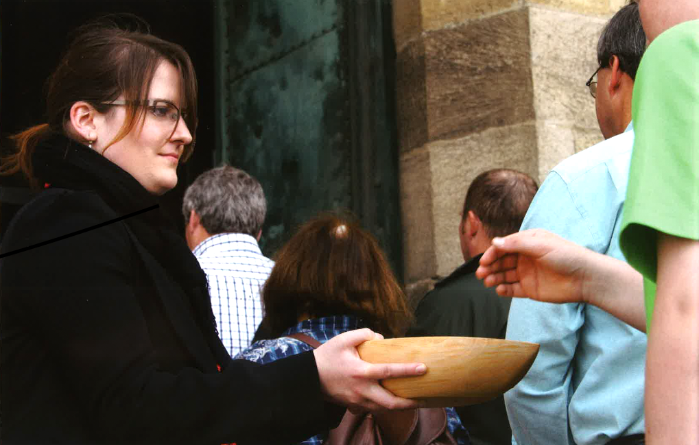 Eine Frau steht mit einer Schale mit Infos für den Gottesdienst am Kirchenportal